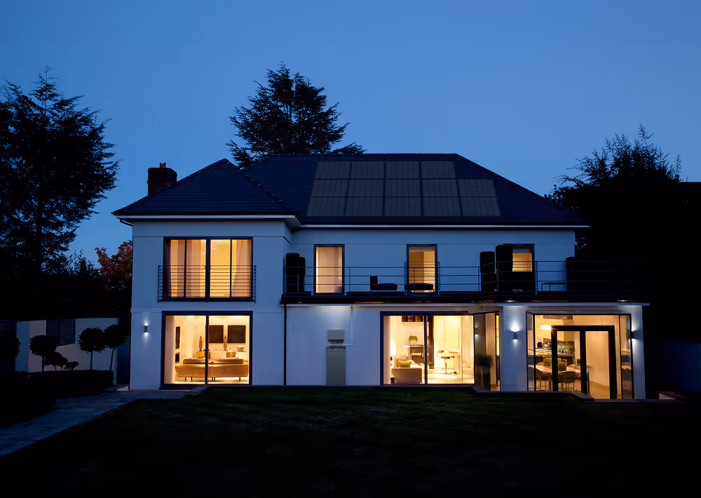 Modern two-story house at dusk with illuminated interior and solar panels on the roof.