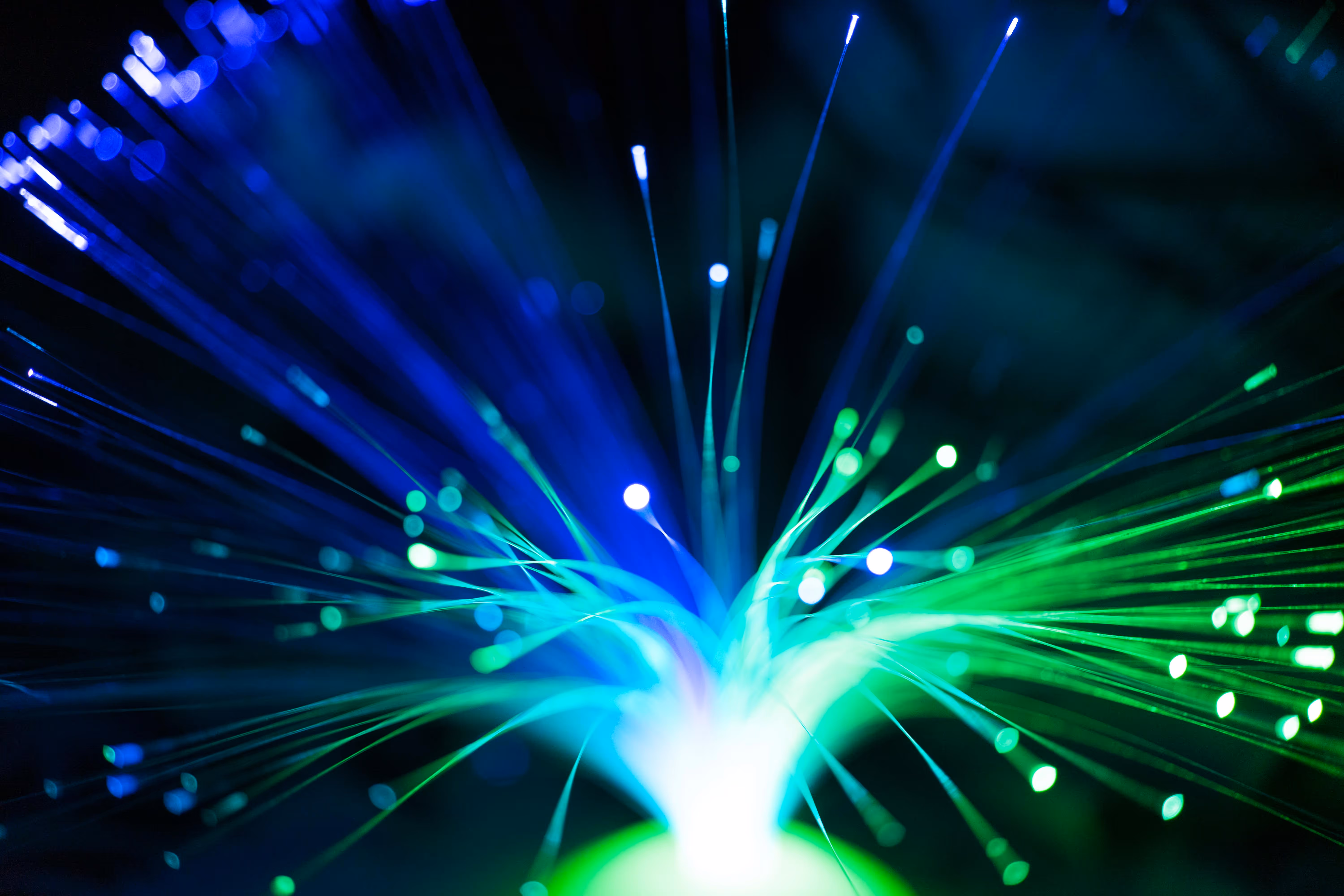 Close-up of blue and green fiber optic light strands glowing on a black background.