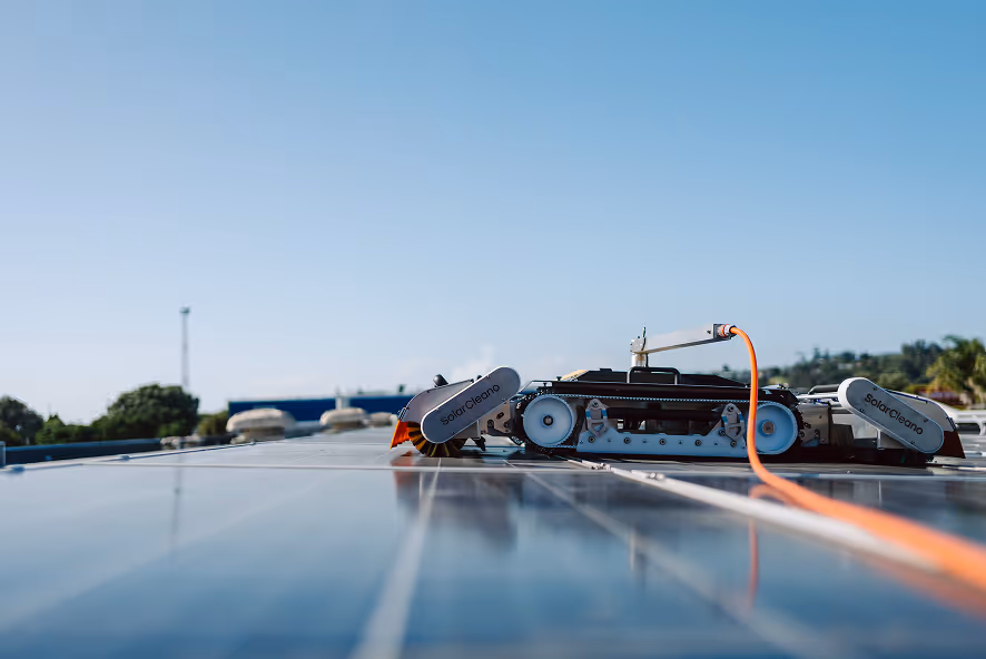 Robot cleaner with SolarClean branding operating on solar panels under a clear blue sky.