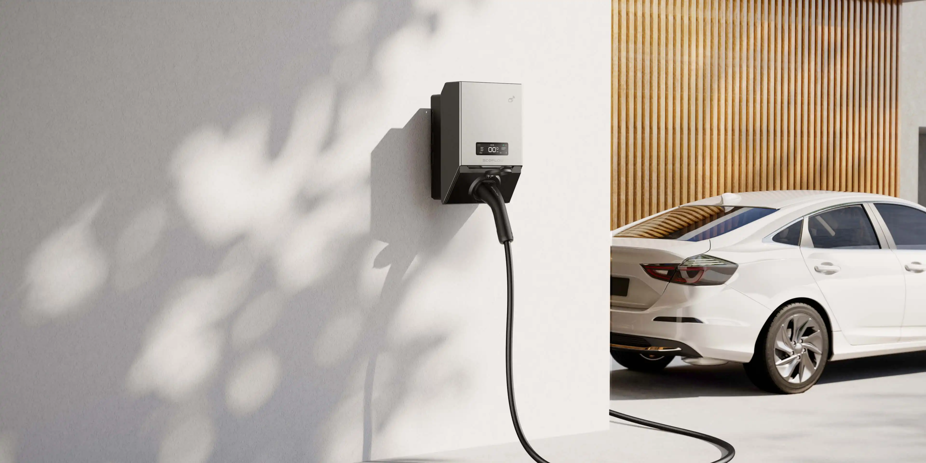 Electric vehicle charger mounted on a white wall with a white car parked nearby in front of a wooden garage door.