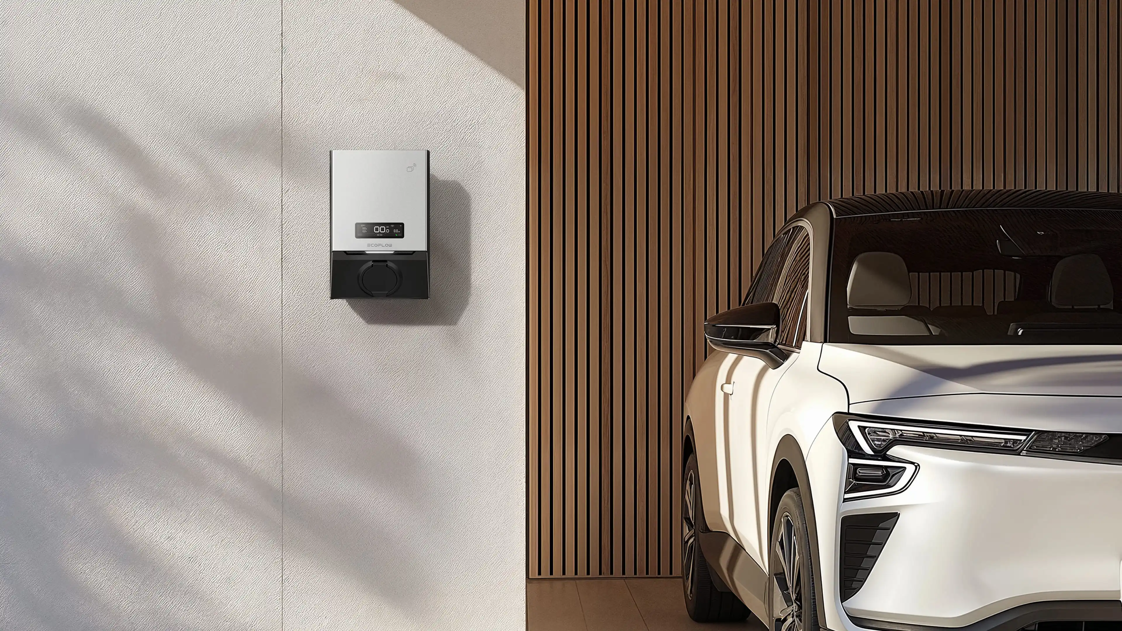 White electric car parked indoors beside a wall-mounted electric vehicle charging station.