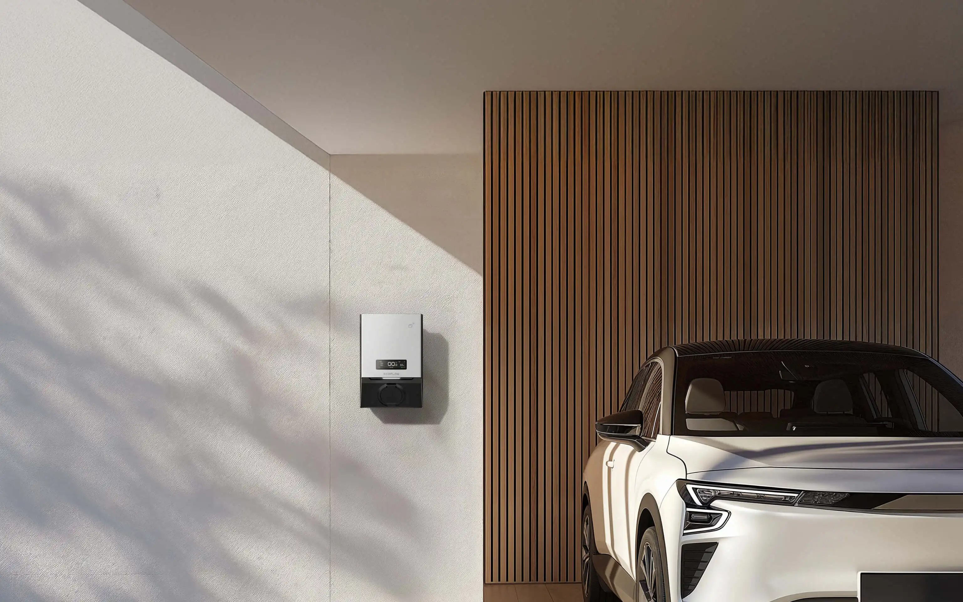 White electric car parked indoors beside a wall-mounted electric vehicle charging station.