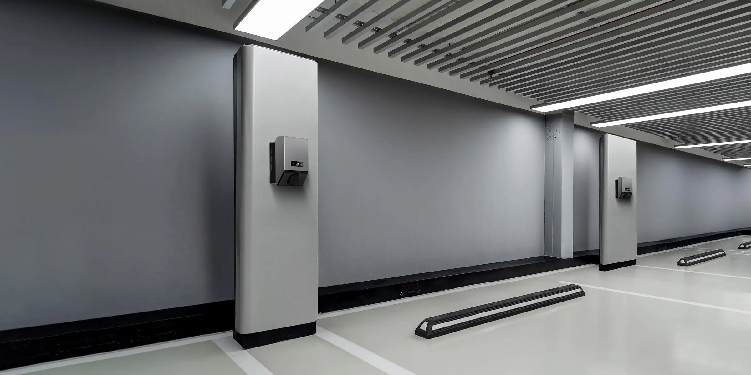 Modern indoor parking with gray walls, ceiling lights, and electric vehicle charging stations mounted on pillars.