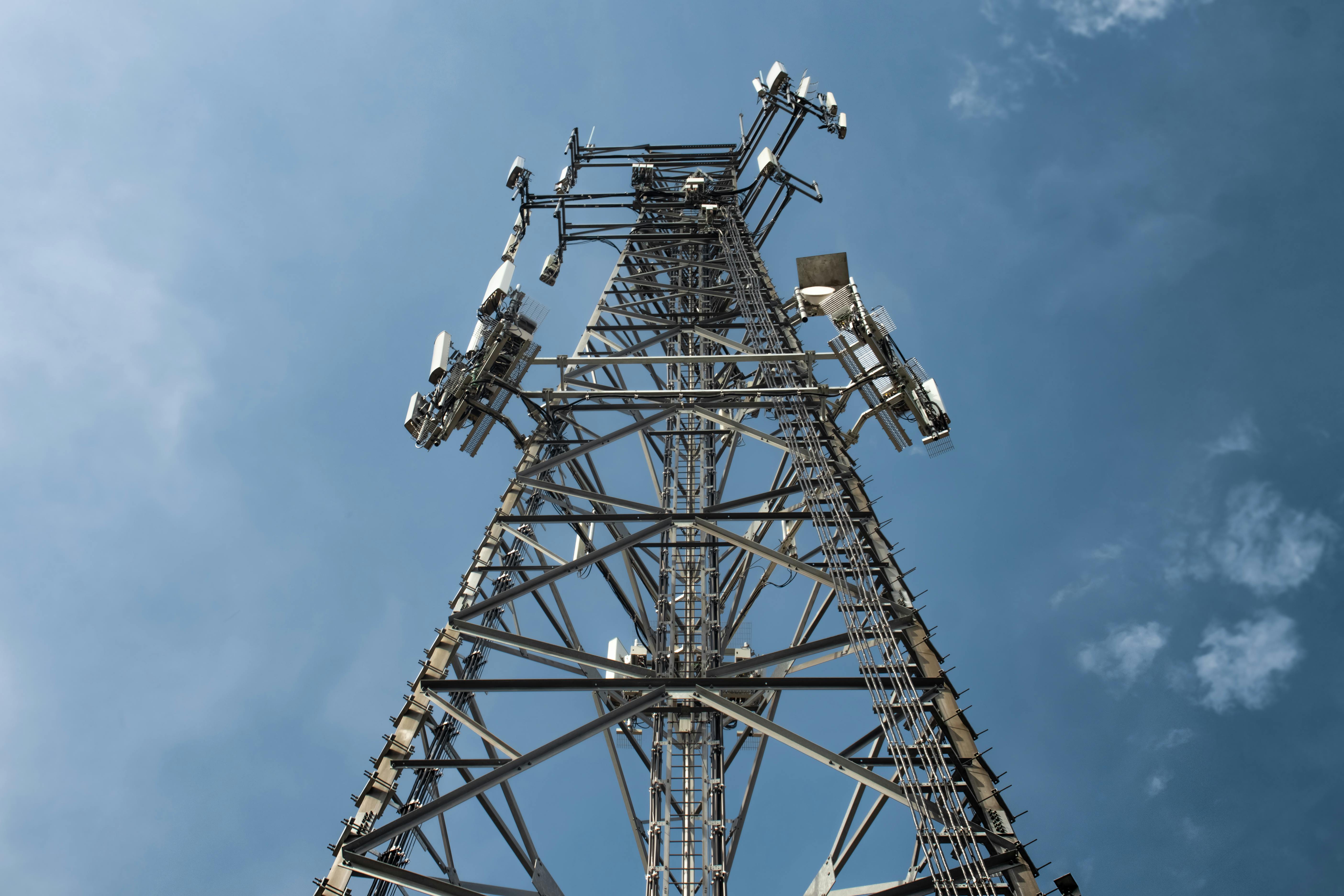Close-up view looking up at a tall metal telecommunications tower against a blue sky.