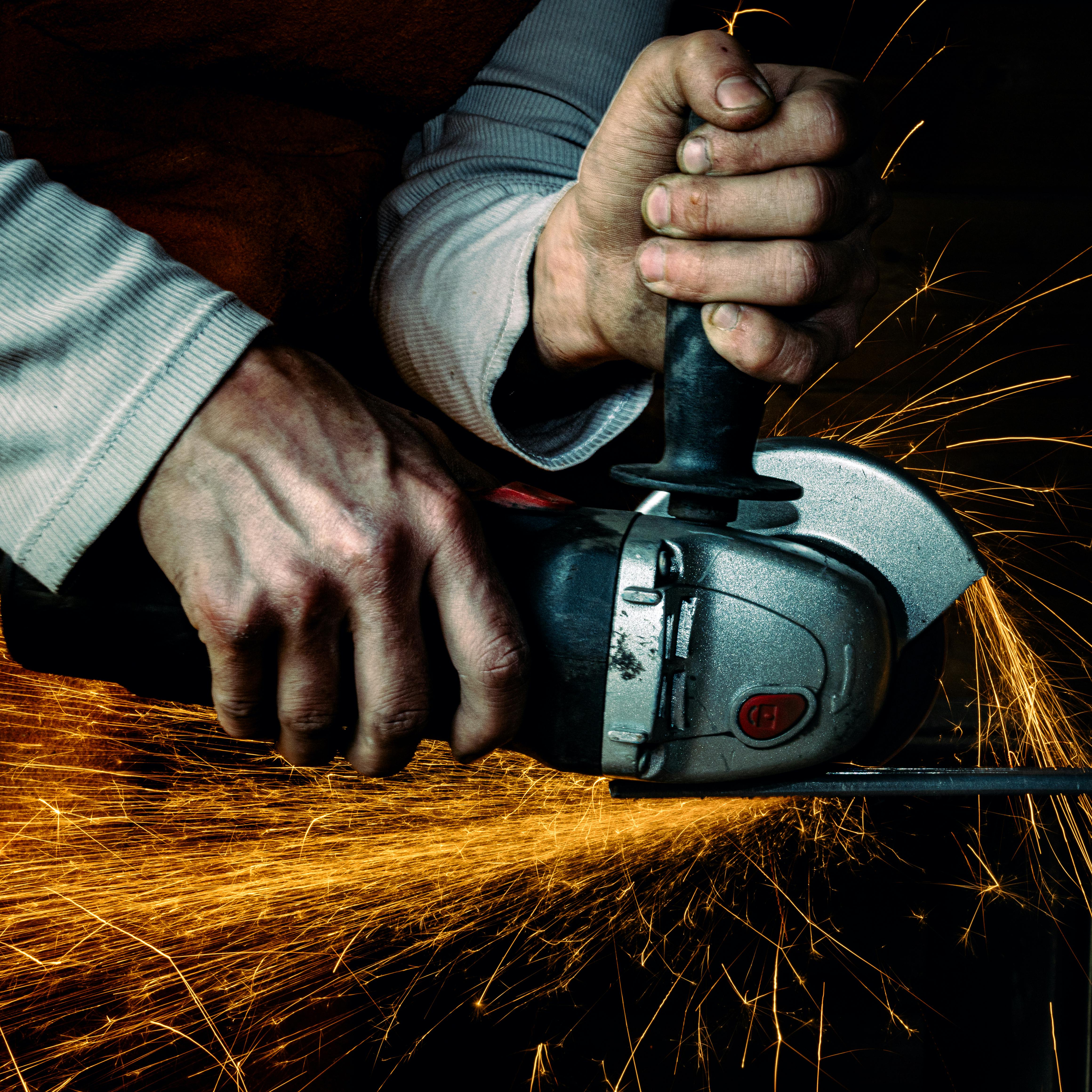 Close-up of hands using an angle grinder producing orange sparks while cutting metal.