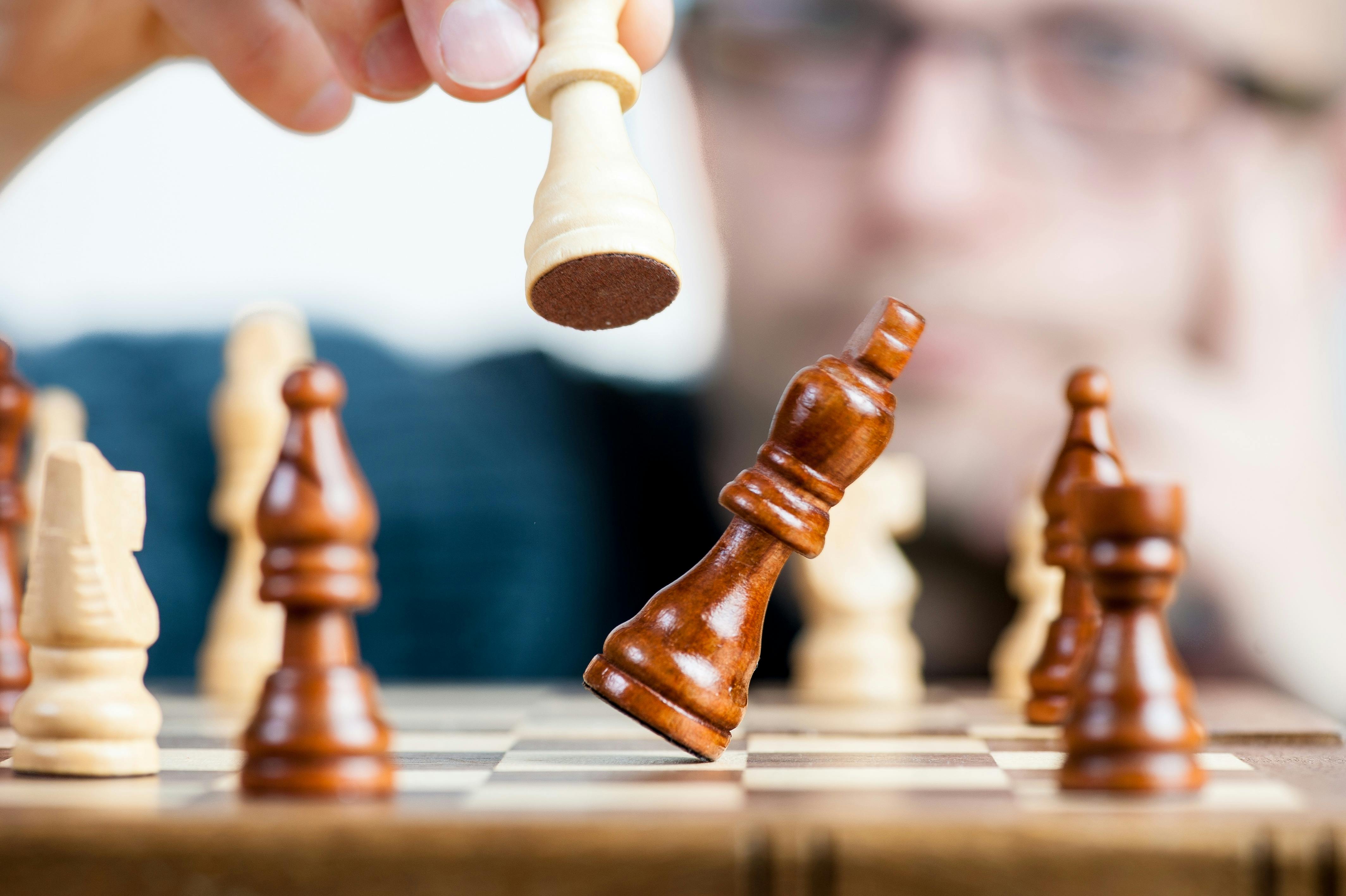 Hand holding a white chess piece capturing a dark brown king piece on a chessboard.