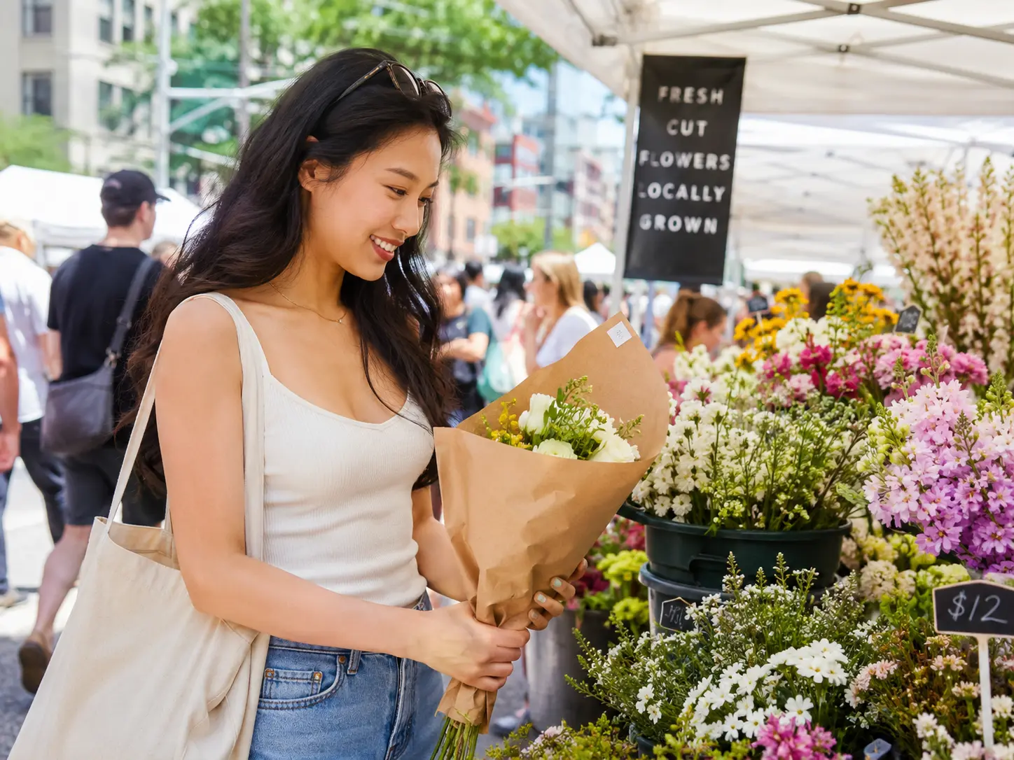 Smiling woman holding a bouquet at an outdoor flower market with various colorful flowers.
