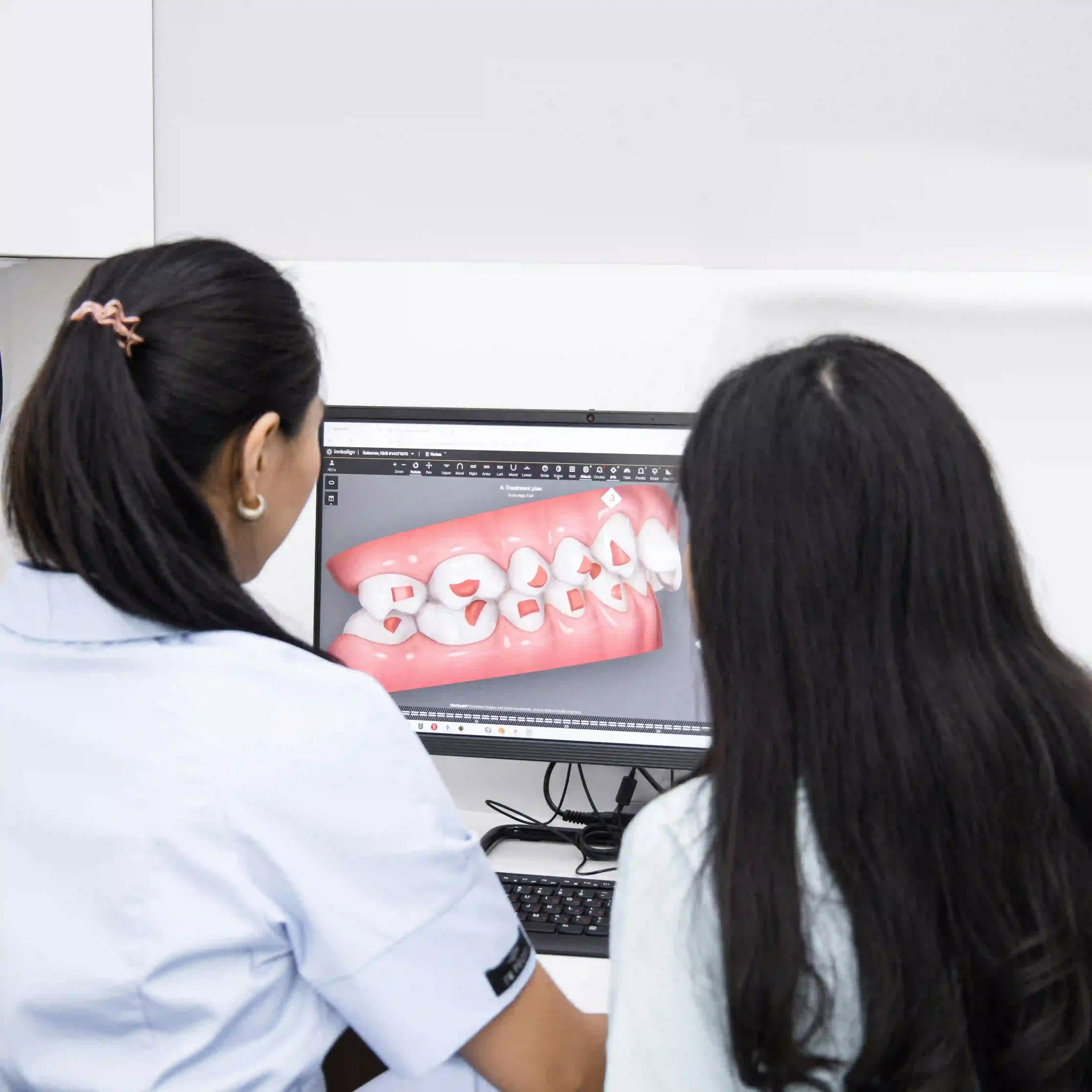 Dentist and patient looking at a digital dental treatment plan showing teeth with markings on a computer screen.