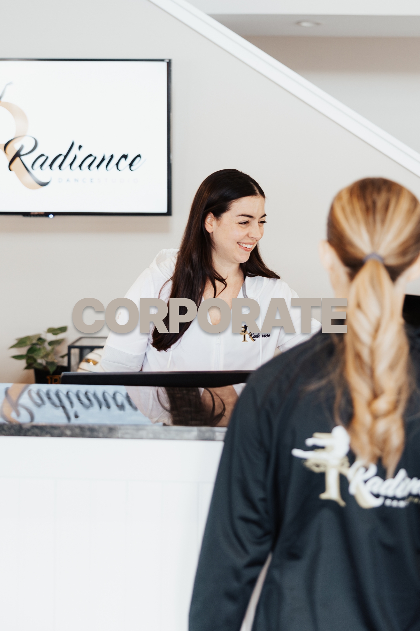 Woman smiling behind a reception desk at Radiance Dance Studio, another woman seen from back.