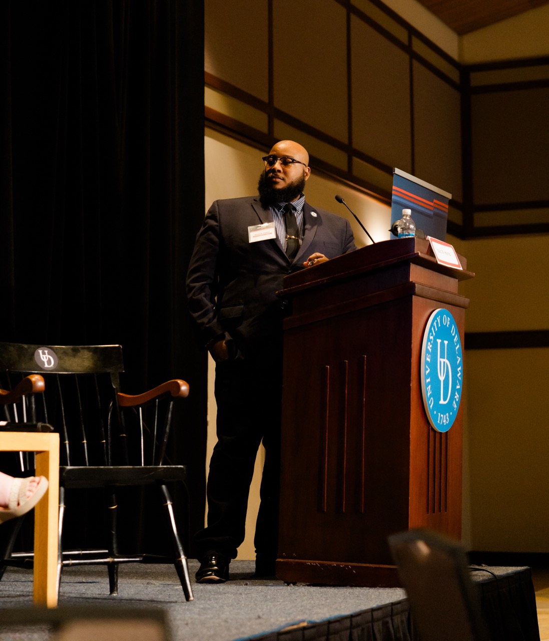Man in suit standing behind University of Delaware podium speaking at an event.
