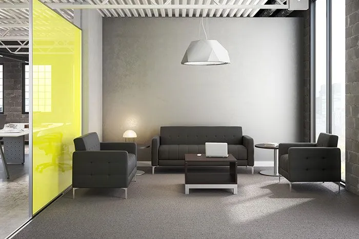 Modern office lounge area with gray sofas, a white geometric pendant light, a laptop on a coffee table, and a large window letting in natural light.