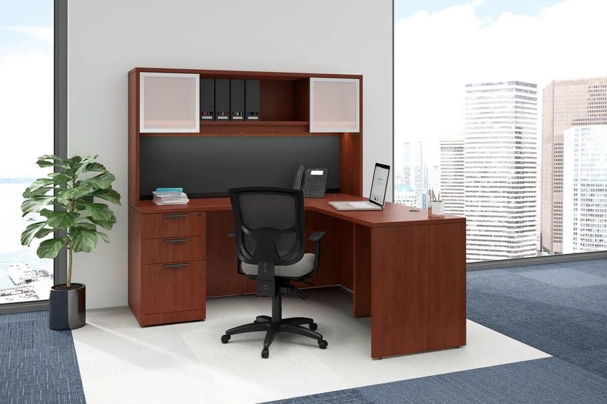Modern office corner desk with wooden finish, black mesh swivel chair, laptop, phone, and office supplies by large windows overlooking cityscape.