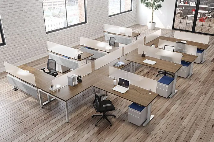 Modern open office space with multiple wooden desks arranged in clusters, featuring ergonomic black chairs, laptops, and minimal office supplies.