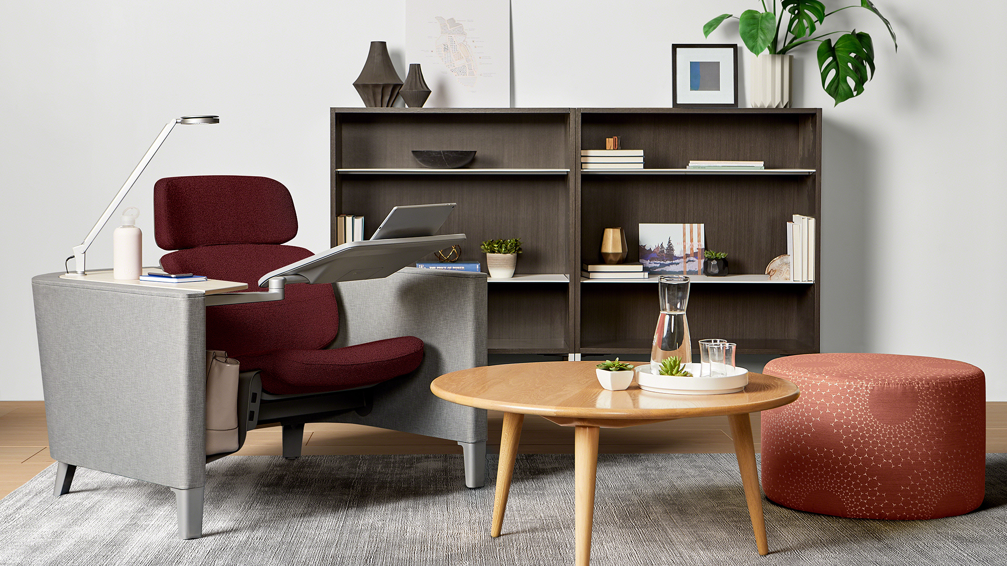 Steelcase lounge seating area with armchair, ottoman, coffee table, and shelving in a modern office workspace