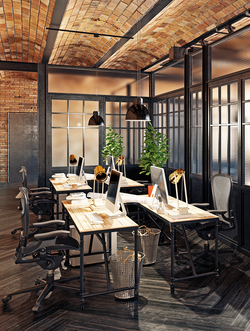 Modern office workspace with wooden desks, desktop computers, ergonomic chairs, green plants, black pendant lights, and brick ceiling.