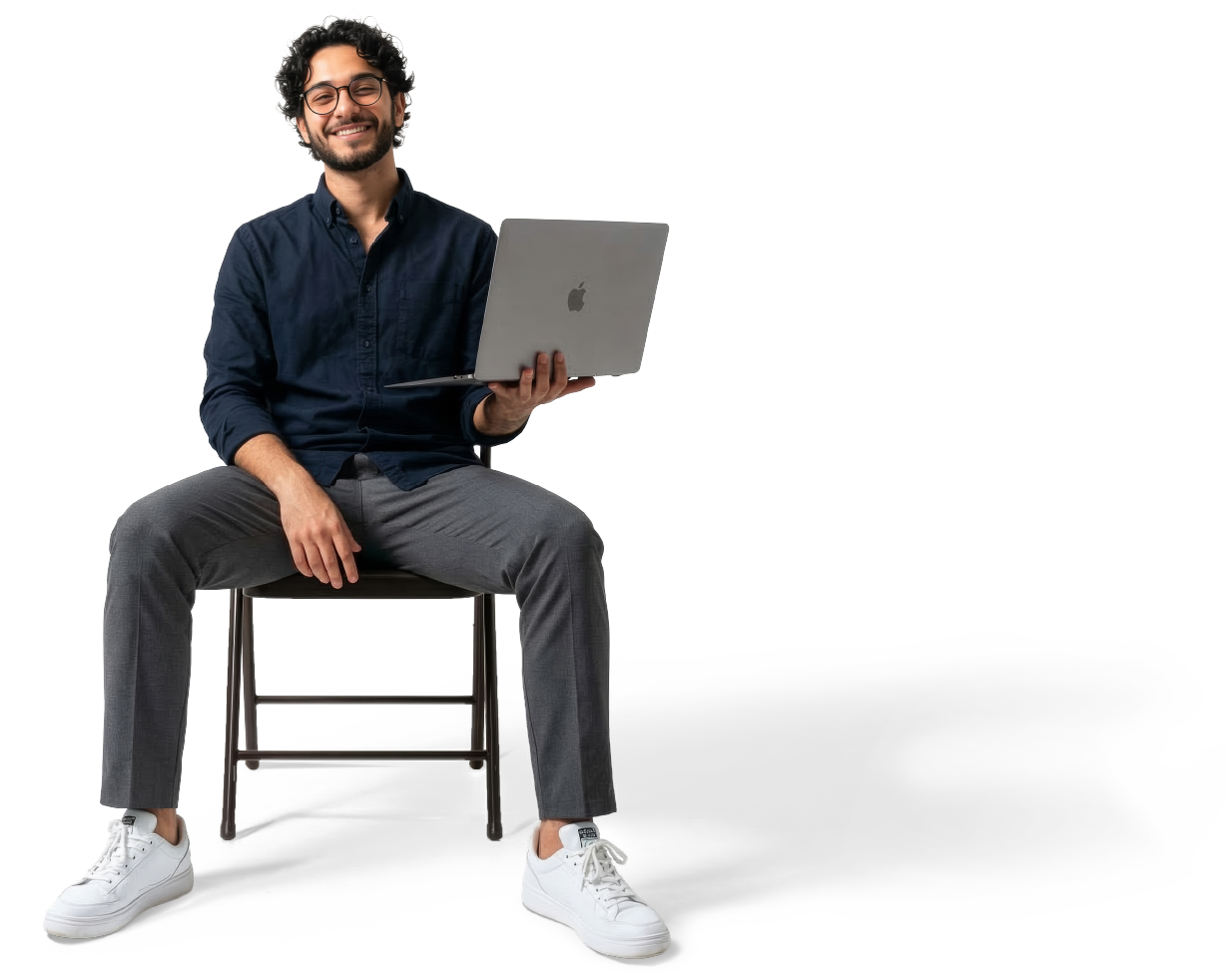 Smiling man wearing glasses sitting on chair holding open laptop in one hand.