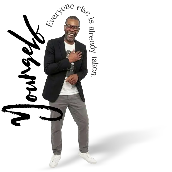 Smiling man with glasses in a black blazer, white shirt, gray pants, and white sneakers.