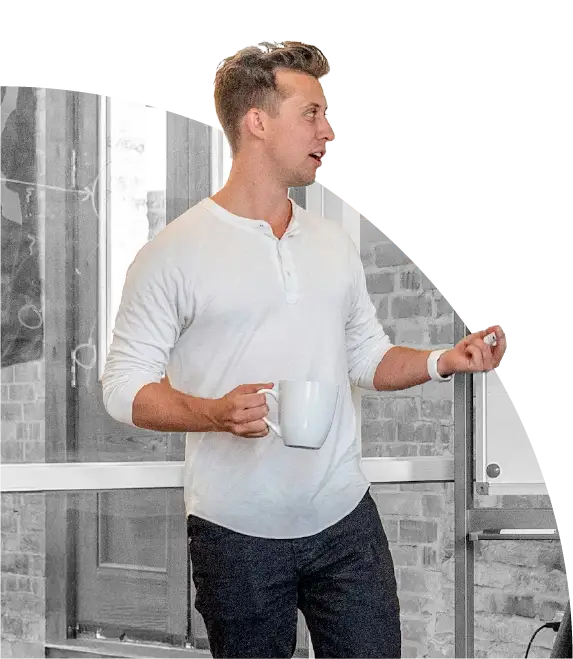 Man in white shirt holding a white mug, gesturing with his other hand in an office setting.