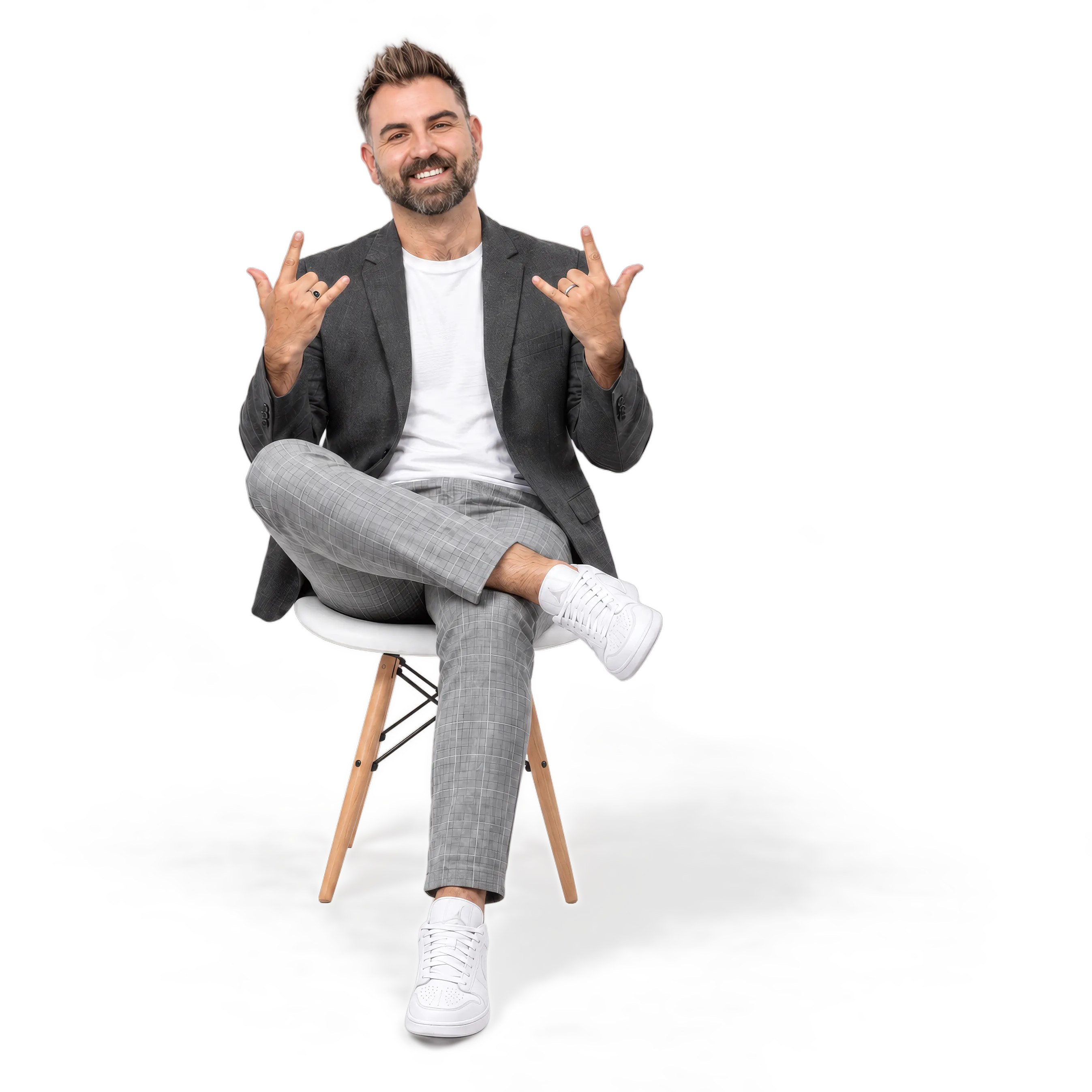 Smiling man in a gray blazer sitting on a white chair, giving rock-on hand gestures with both hands.