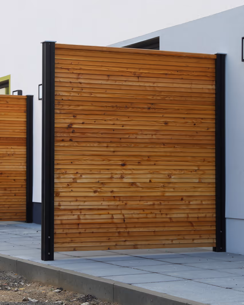 Holzzaun aus horizontalen Latten mit schwarzen Metallpfosten vor moderner Hausfassade.
