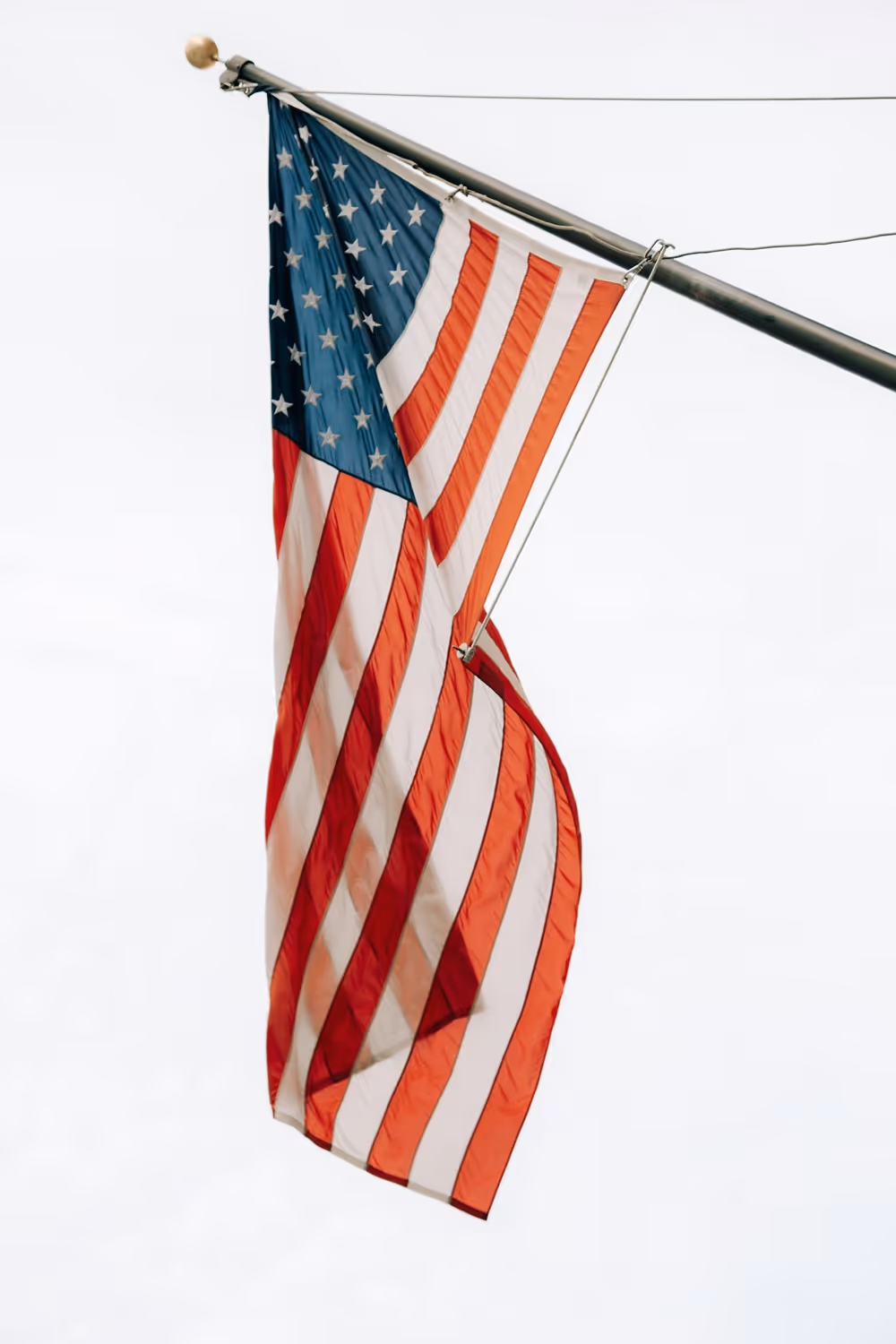 American flag hanging down from a flagpole against a clear sky.