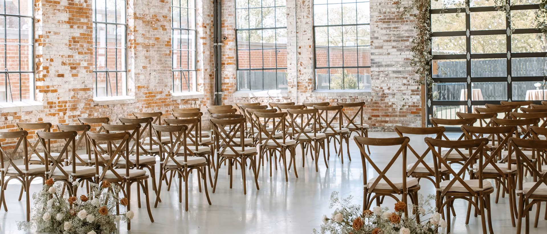 Rows of brown wooden chairs with cushions set up in a bright room with large windows and brick walls.