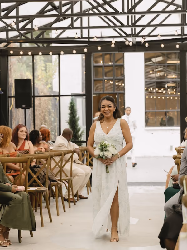 Bright, airy event space with greenery hanging from black metal beams and tables covered with white cloth.