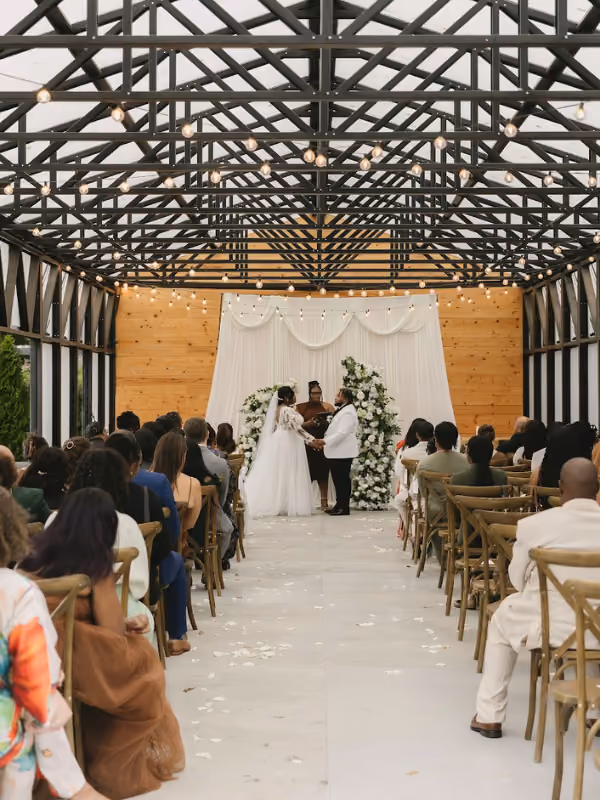 Bright, airy event space with greenery hanging from black metal beams and tables covered with white cloth.