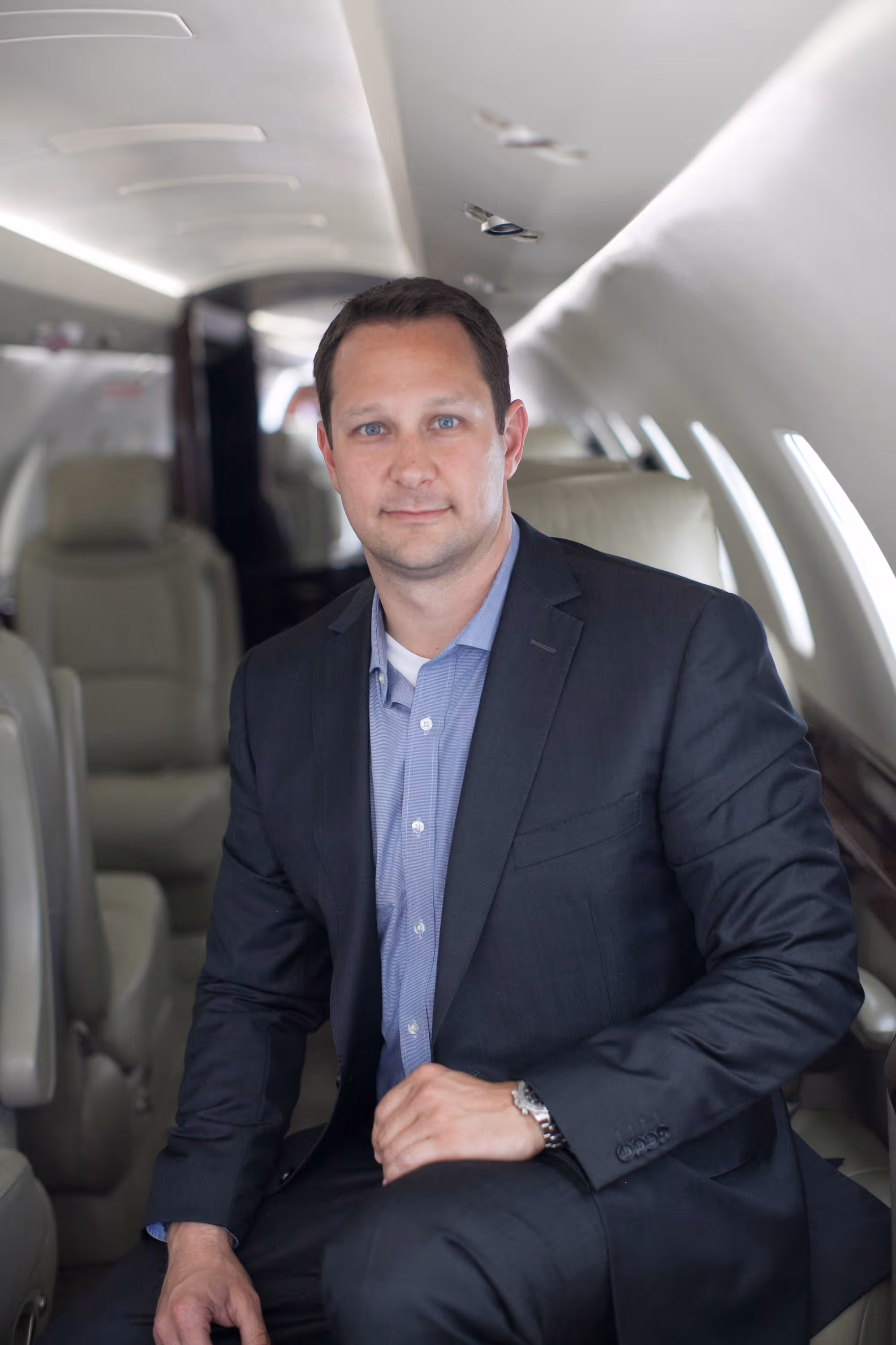 Man in a dark suit and blue shirt sitting inside a private jet cabin.