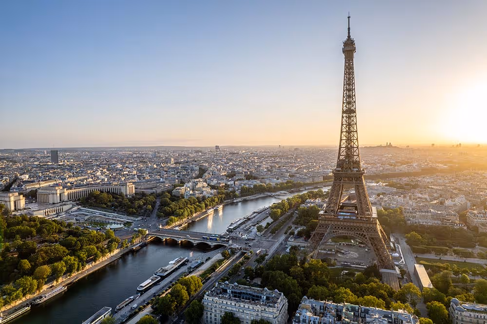 Aerial view of the Eiffel Tower at sunset with the Seine River and Paris cityscape.