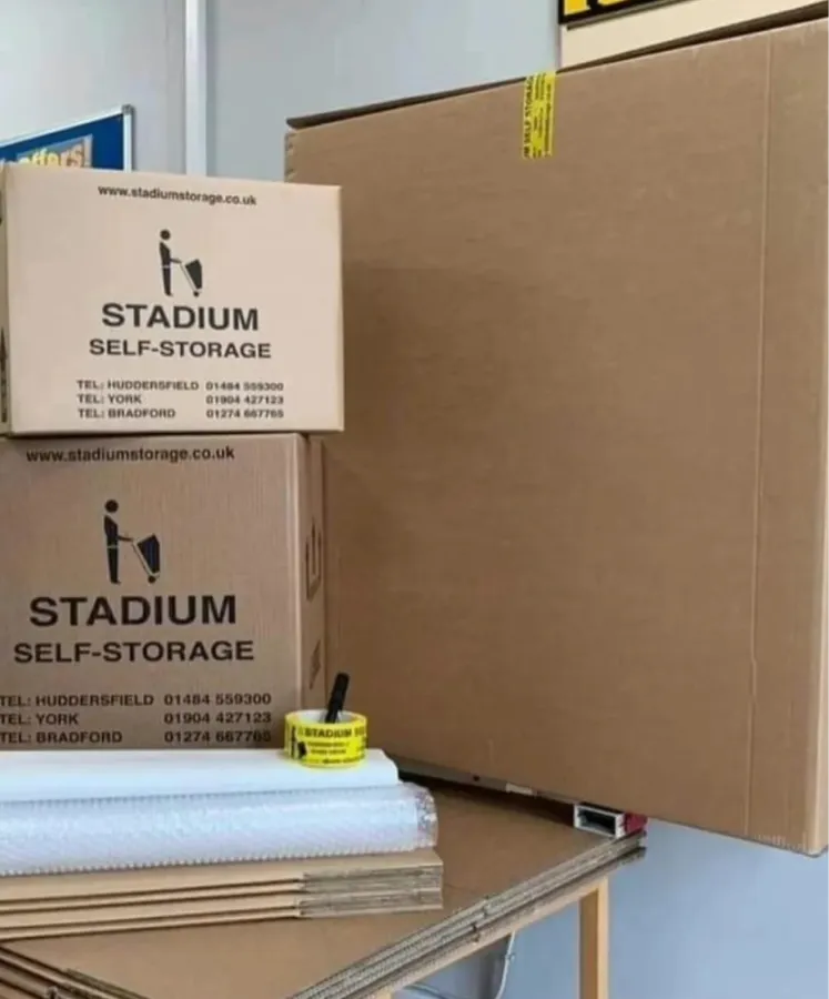 Stack of cardboard boxes and packing materials labeled Stadium Self-Storage with contact numbers for Huddersfield, York, and Bradford.