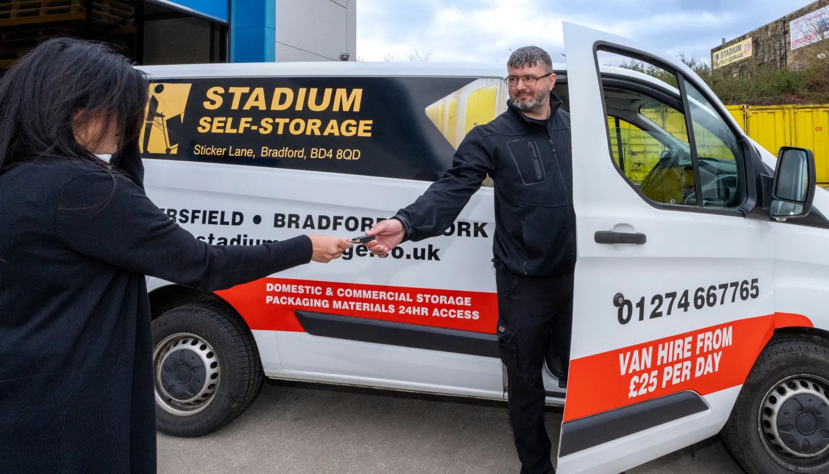 Man standing in white van door handing a key to a woman, van advertises Stadium Self-Storage and van hire for £25 per day.