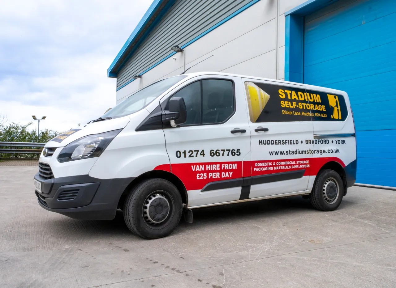 White van with Stadium Self-Storage branding parked outside a blue warehouse door.