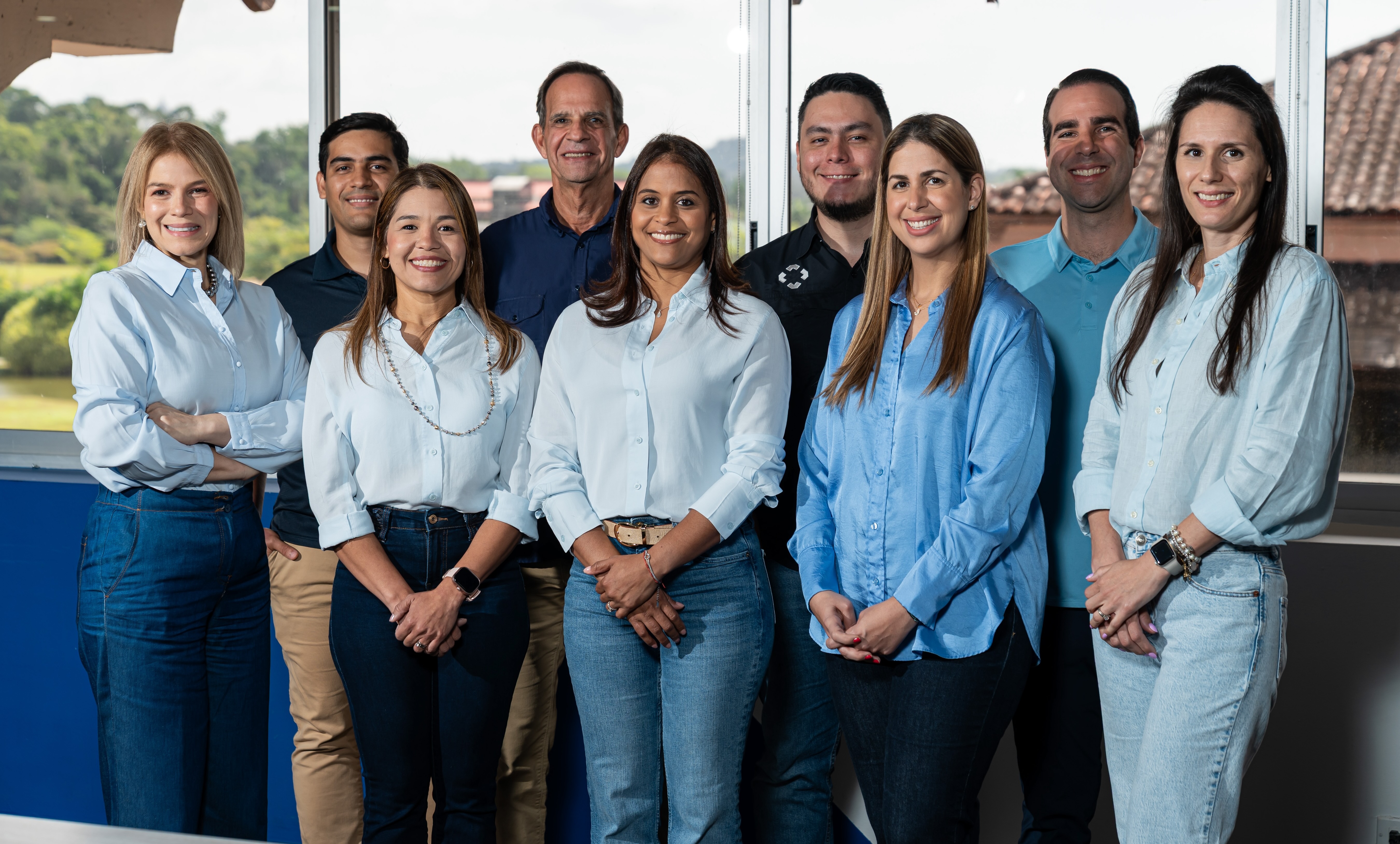 Foto grupal de directores de Maxia sonrientes de pie, frente a unos grandes ventanales con vistas a un paisaje verde en el exterior.