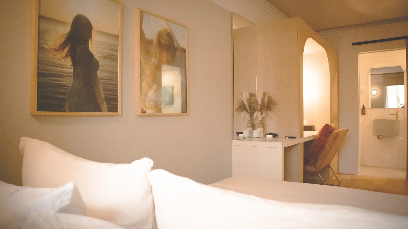 Hotel bedroom at La Maison Ralia Montreal with white linens, framed prints and an arched doorway to the bathroom