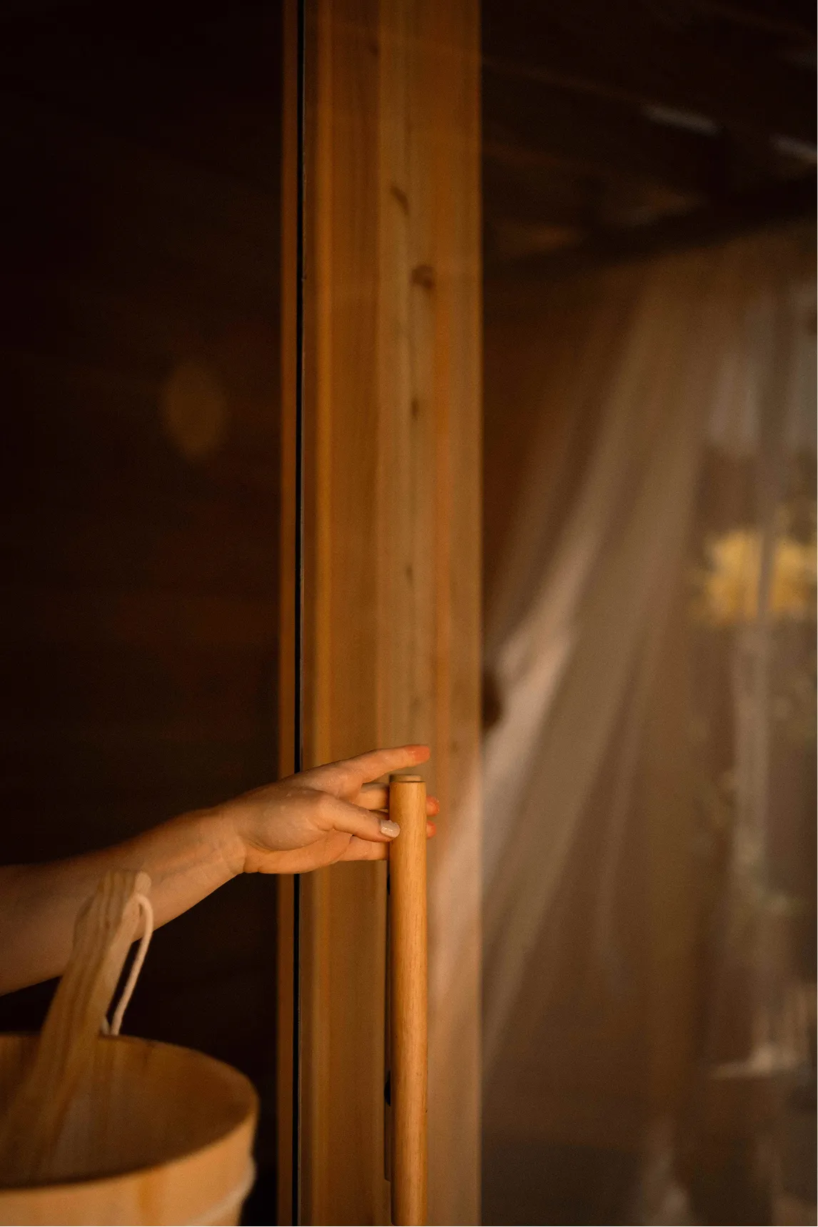 Hand reaching for the wooden handle of the cedar sauna door at La Maison Ralia Montreal