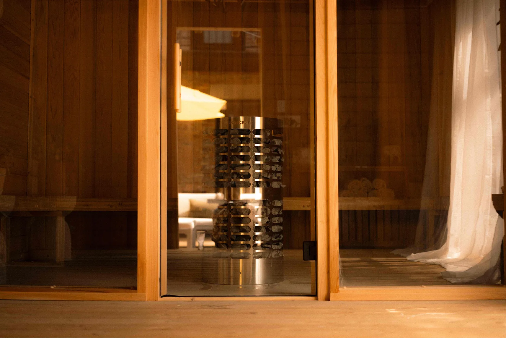 Glowing cedar sauna with a stone heater seen through the glass door at La Maison Ralia in Montreal