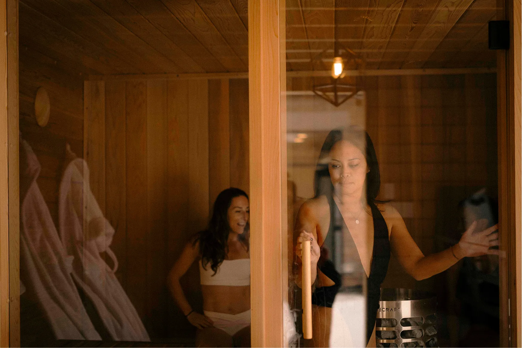 Two guests stepping into the cedar sauna at La Maison Ralia in Montreal, robes hanging by the door