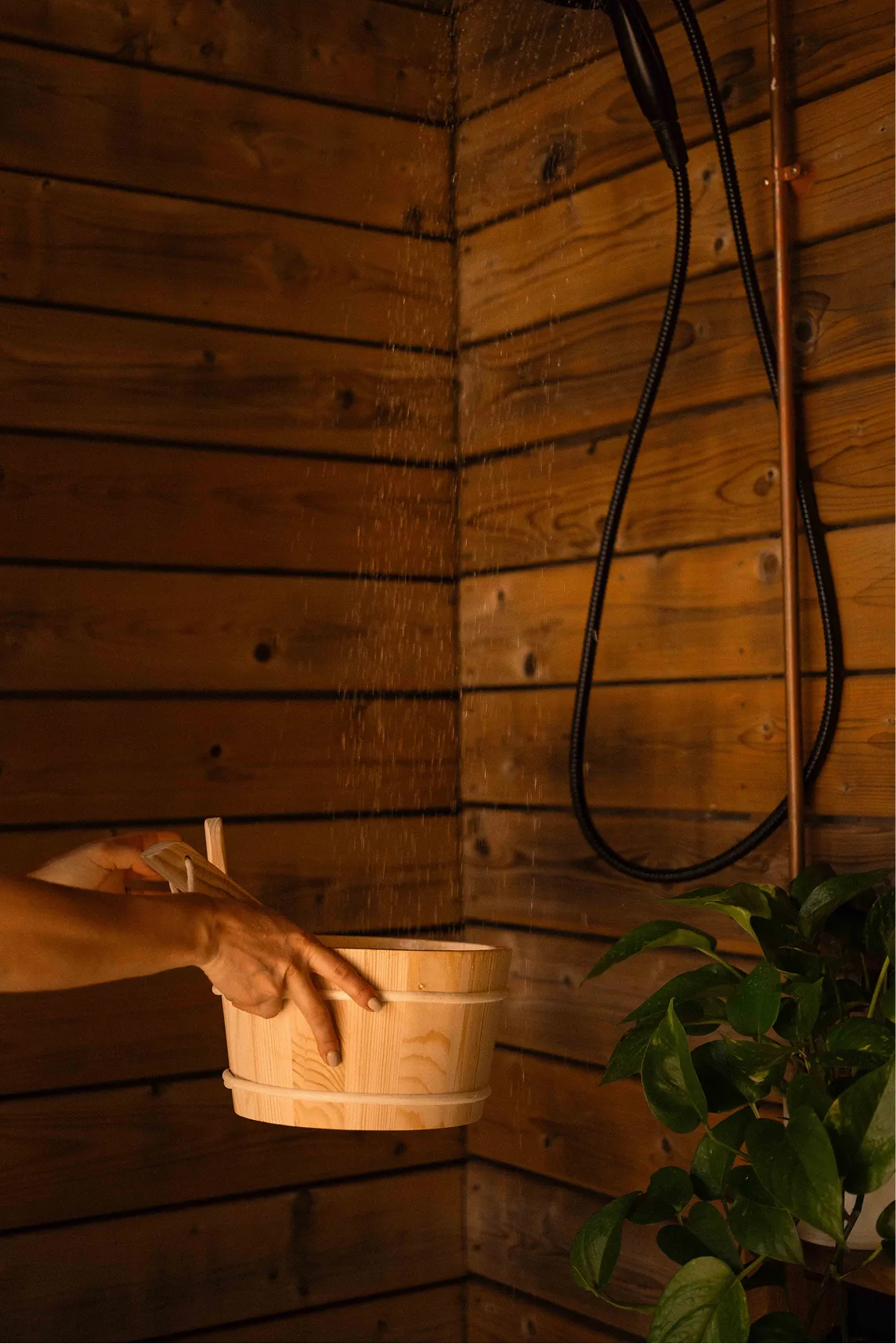 Guest filling a wooden bucket under the rain shower beside the cedar sauna at La Maison Ralia