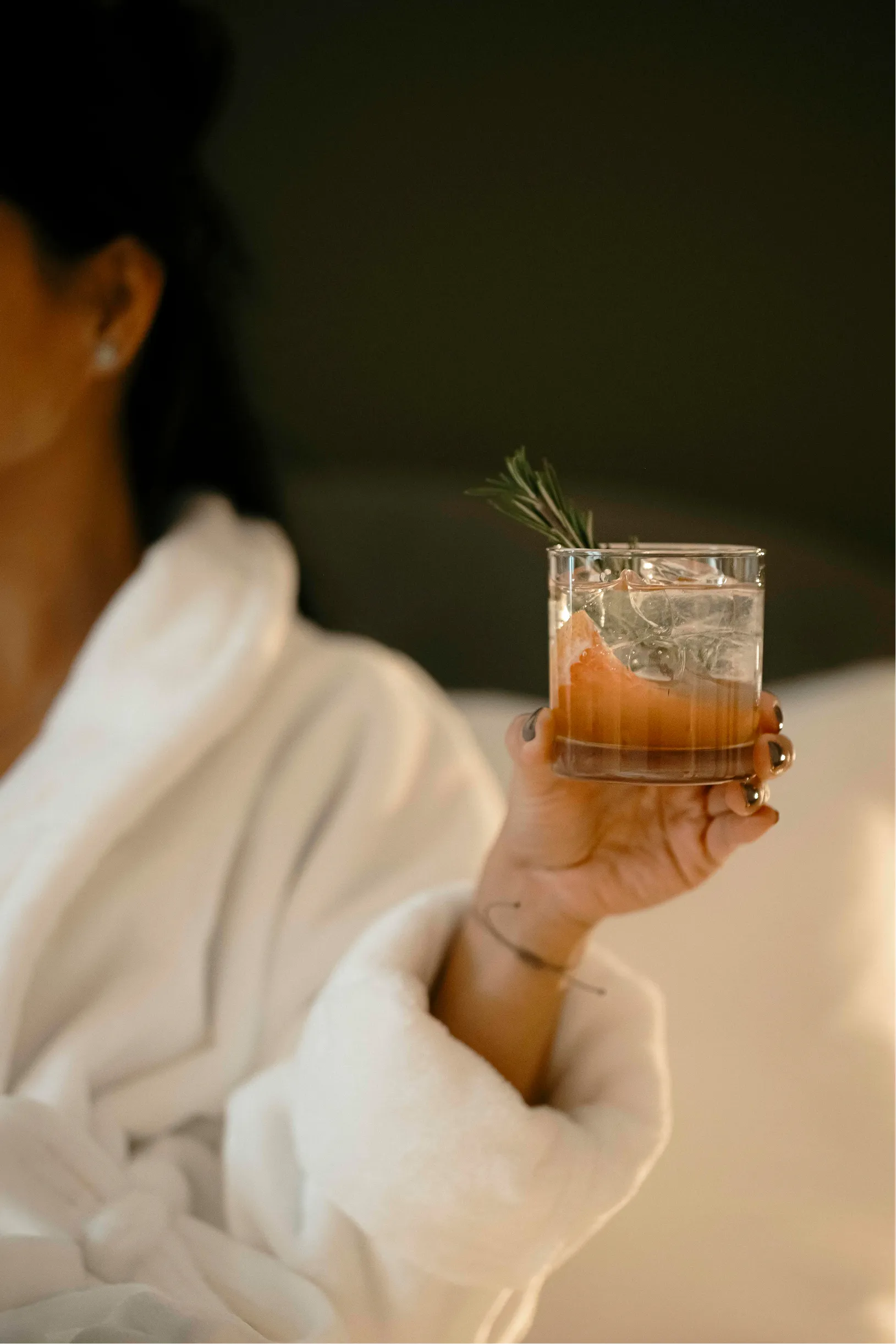 Guest in a white bathrobe holding a rosemary-garnished cocktail at La Maison Ralia in Montreal