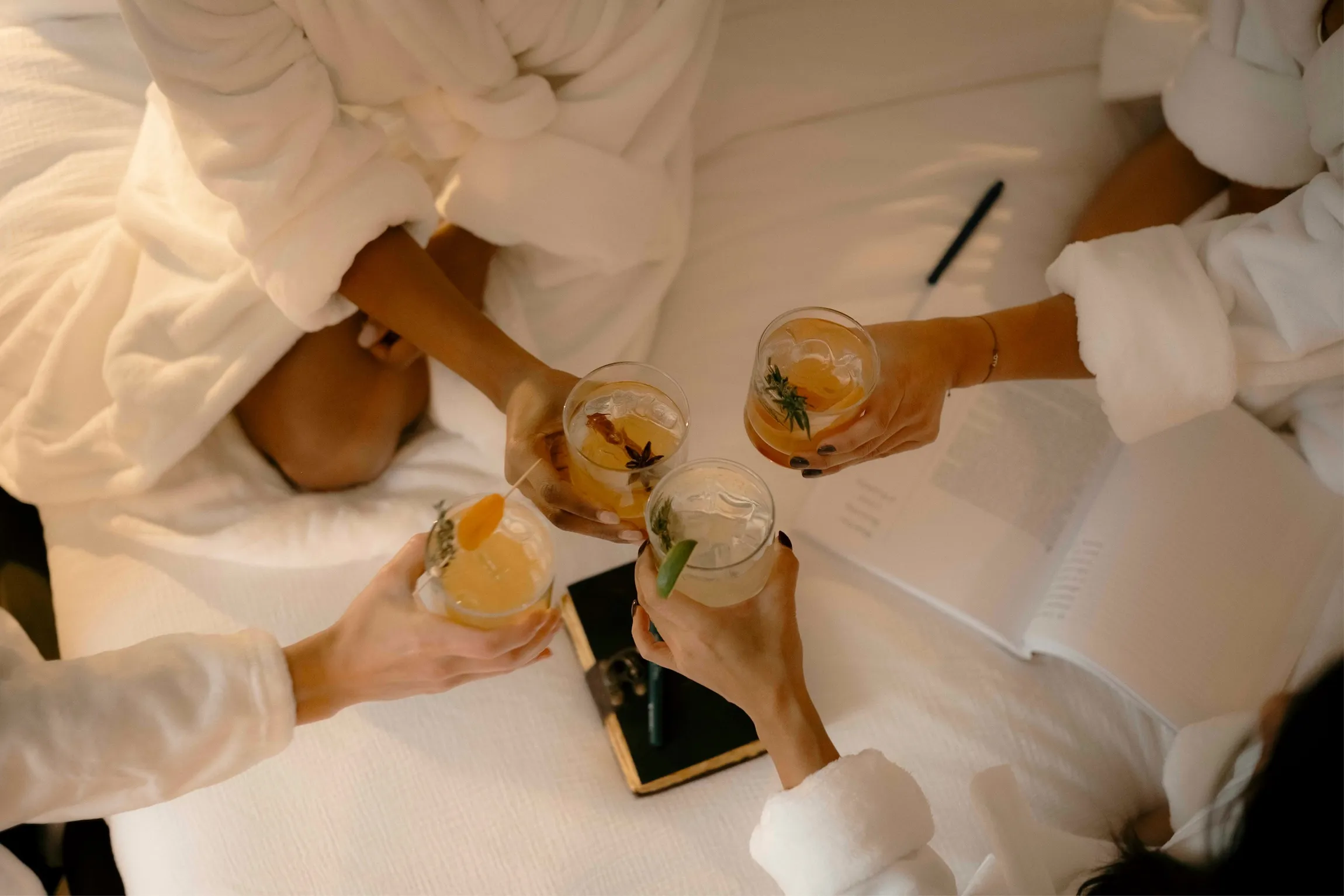 Guests in white bathrobes toasting cocktails on a bed at La Maison Ralia's Montreal boutique hotel