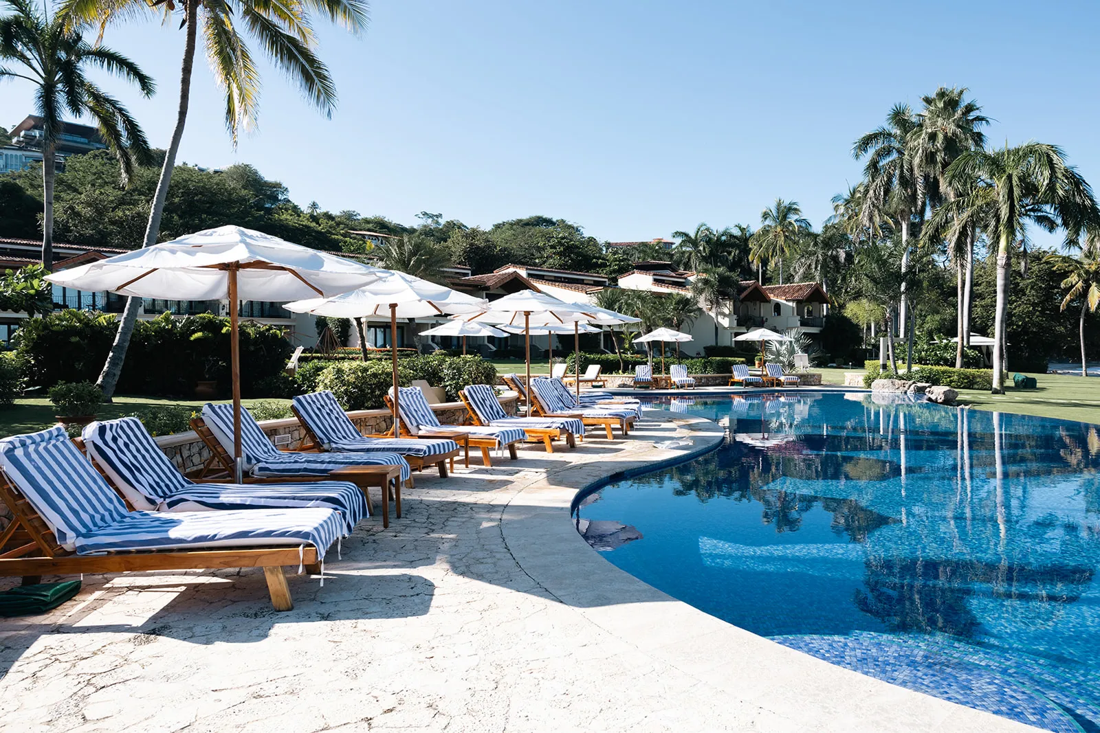 Blue-striped loungers and shade umbrellas lining the palm-fringed pool at the Guanacaste retreat