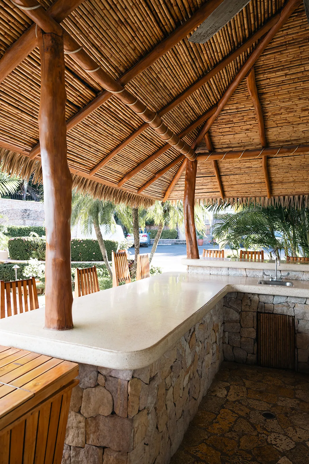 Thatched palapa bar with a stone counter and wooden stools beside the retreat's tropical gardens
