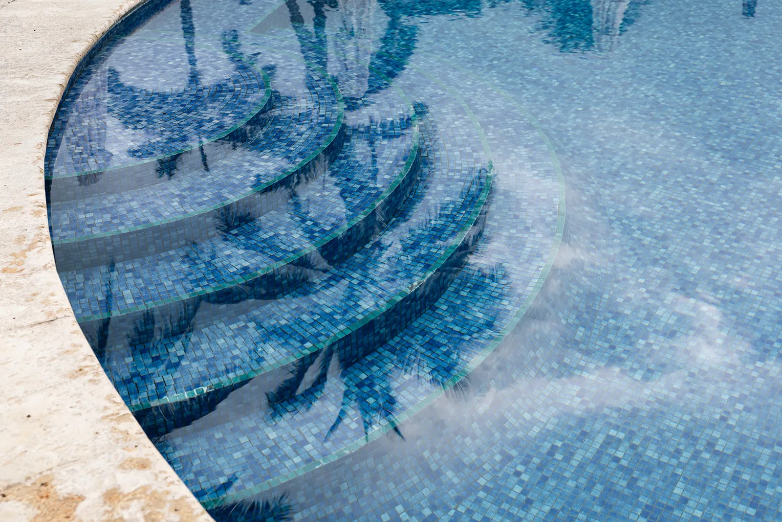 Palm trees reflected in the blue mosaic tile of the pool's curved entry steps