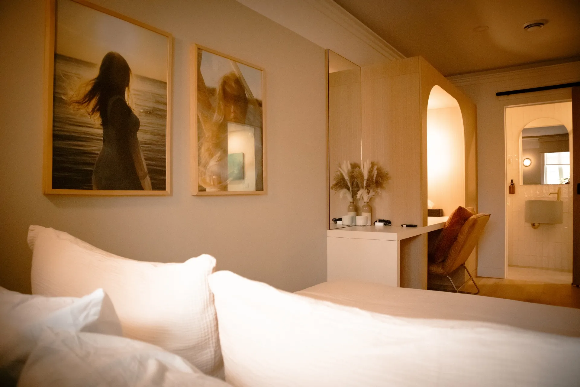 Guest room 104 at La Maison Ralia Montreal with a rust armchair, white desk and framed beach prints above the bed