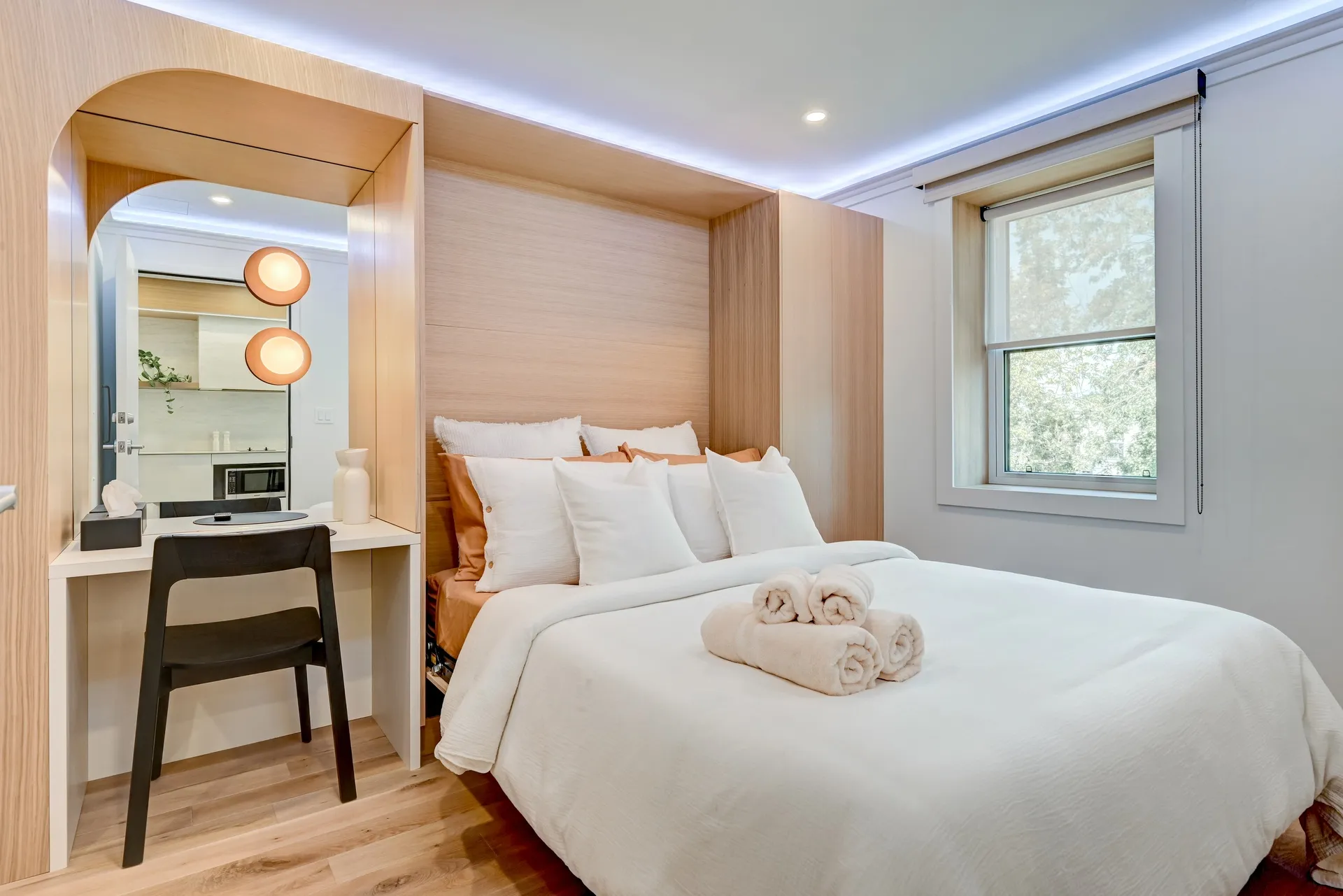 Queen bed with rolled towels beside a mirrored vanity nook in a guest room at La Maison Ralia Montreal