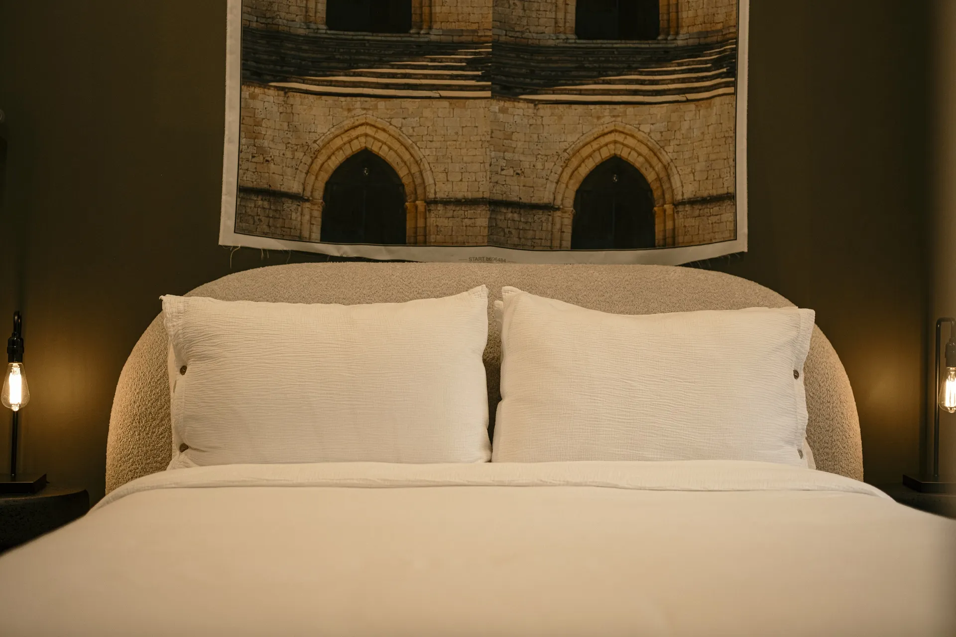 Bed made with crisp white linens under framed archway artwork in a Ralia guest room