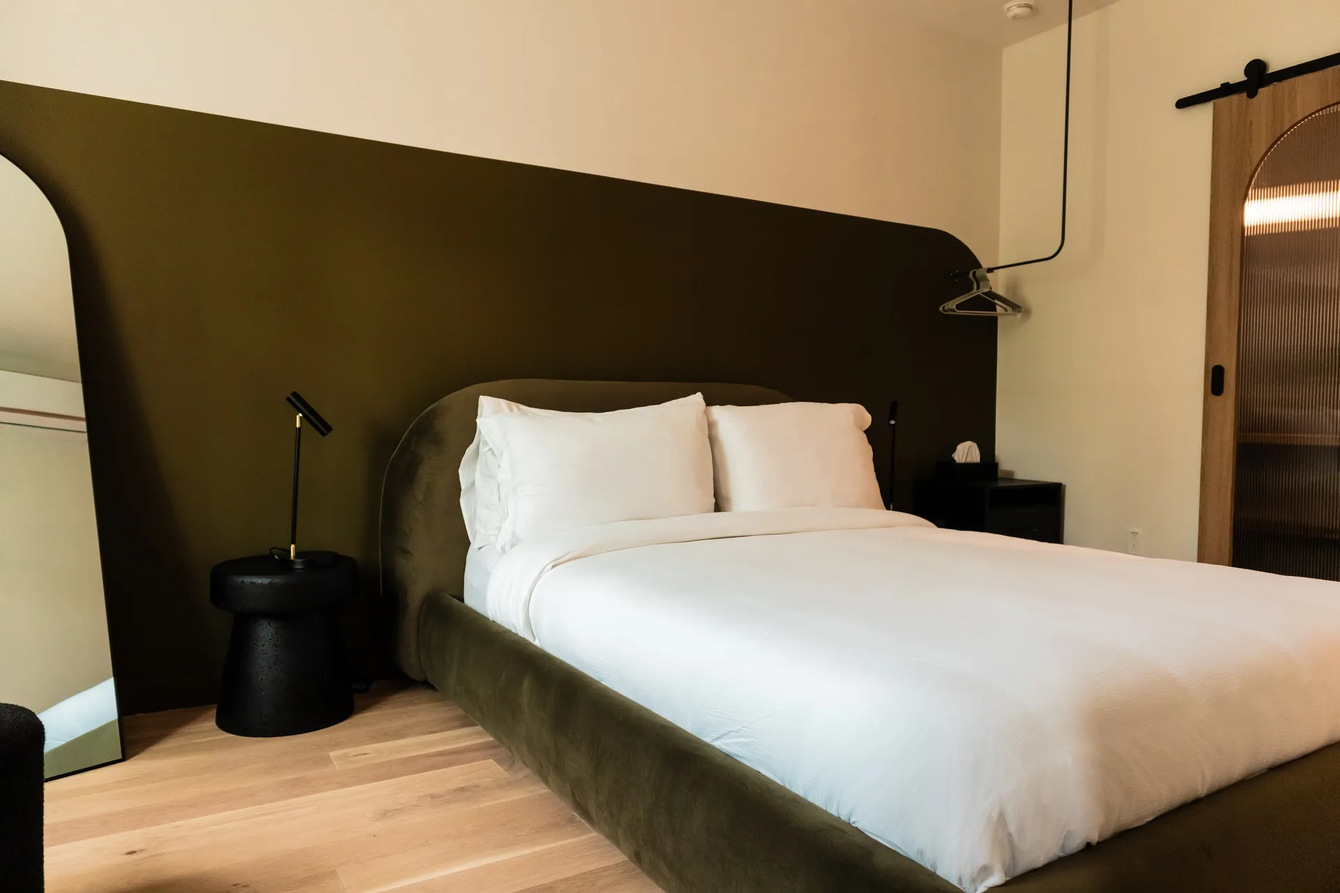 Queen bed with olive upholstered headboard and matching accent wall in a La Maison Ralia guest room