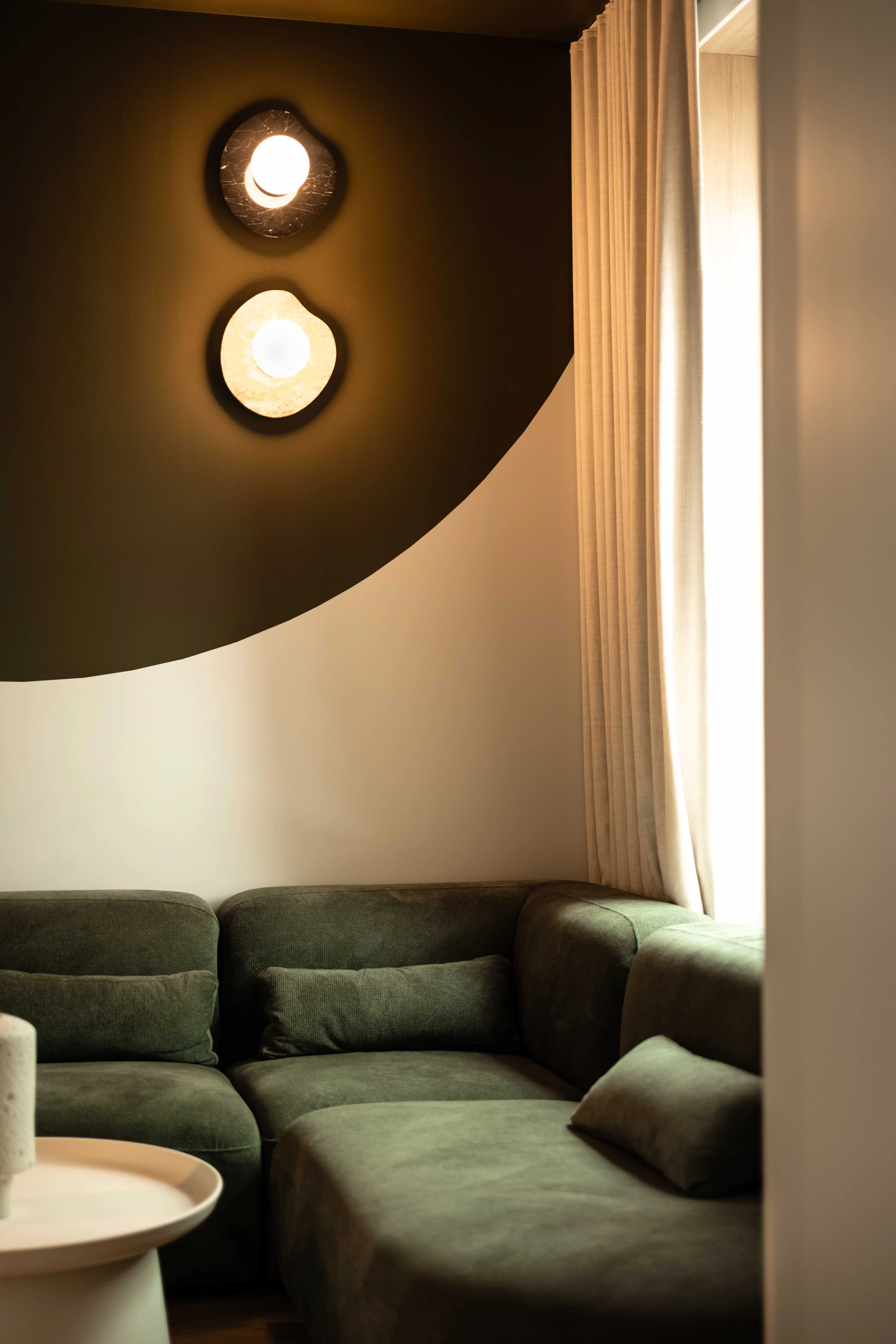 Green velvet sectional sofa beneath a curved olive wall and two glowing sconces at La Maison Ralia Montreal