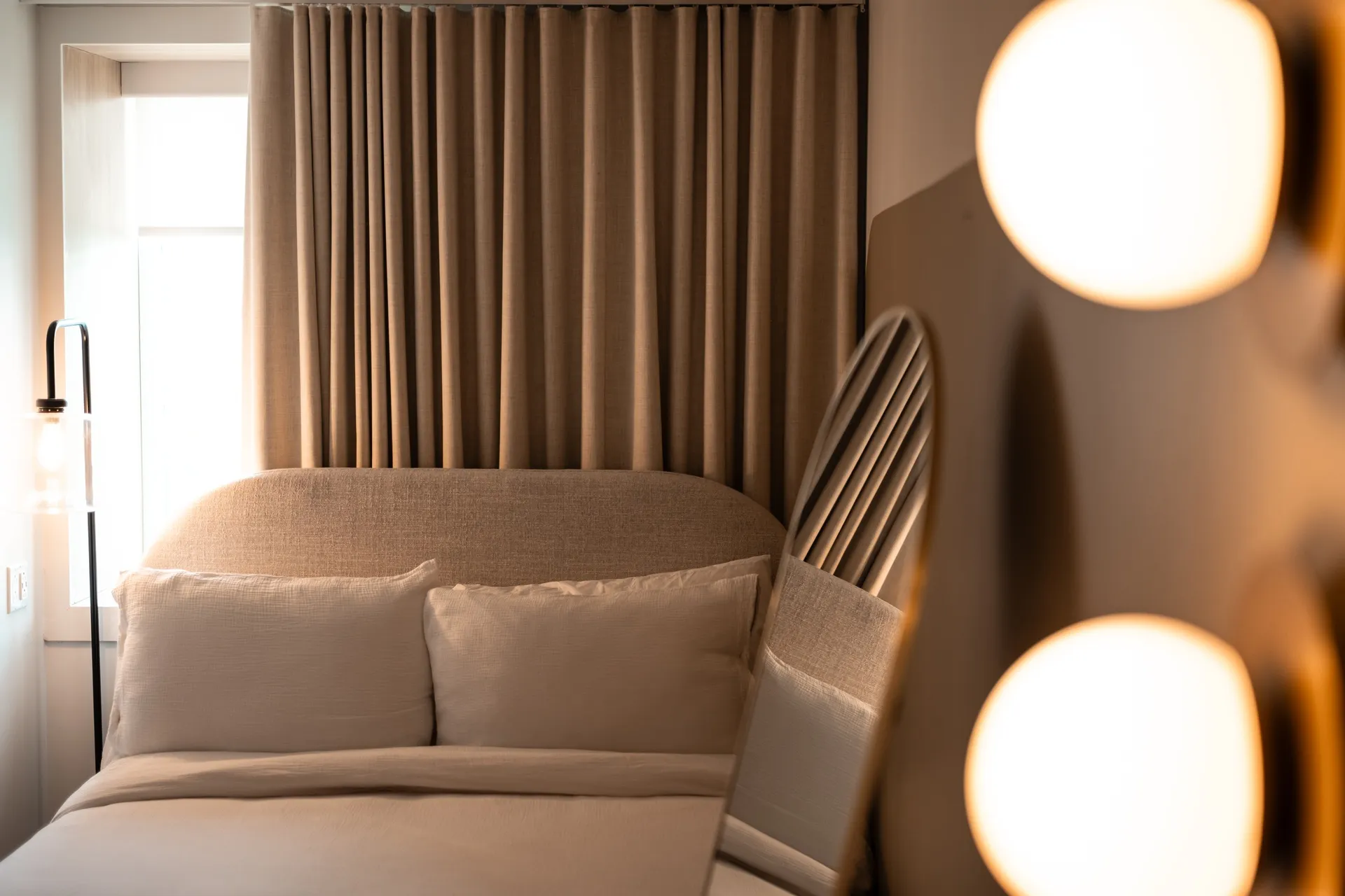 Made bed with linen headboard and warm round lights in a Ralia boutique hotel guest room
